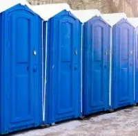 Row of blue portable toilets lined up outdoors in winter snow