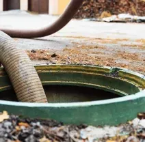 Flexible hose entering a green underground tank opening on a leaf-covered surface