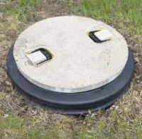 Round white utility cover with two handles set in grassy ground, black rim visible