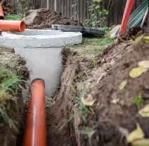Orange pipes in a trench leading to a concrete utility box outdoors