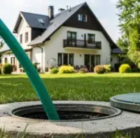 Green hose over a round manhole cover in a lawn, with a white house in the background