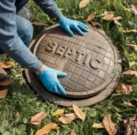 Person in blue gloves lifting a SEPTIC manhole cover in a grassy area with fallen leaves
