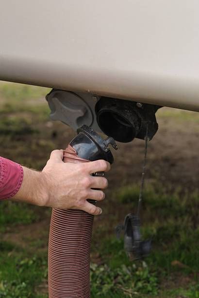 Hand connecting a hose to a vehicle undercarriage near muddy ground