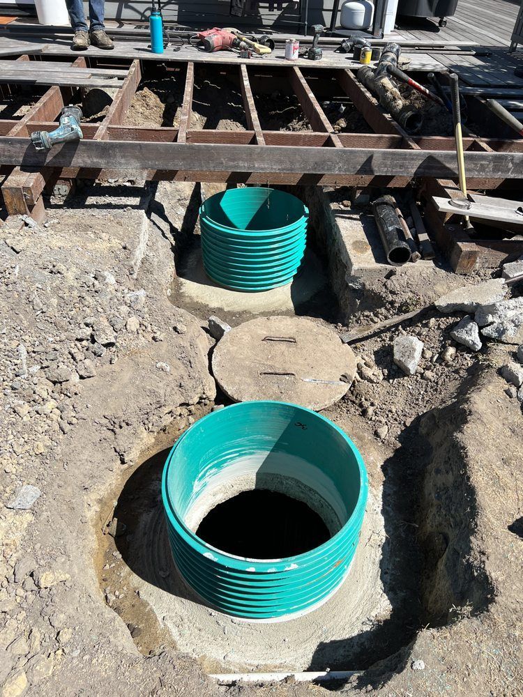 Two green corrugated pipes installed in a dirt trench beneath a wooden deck.
