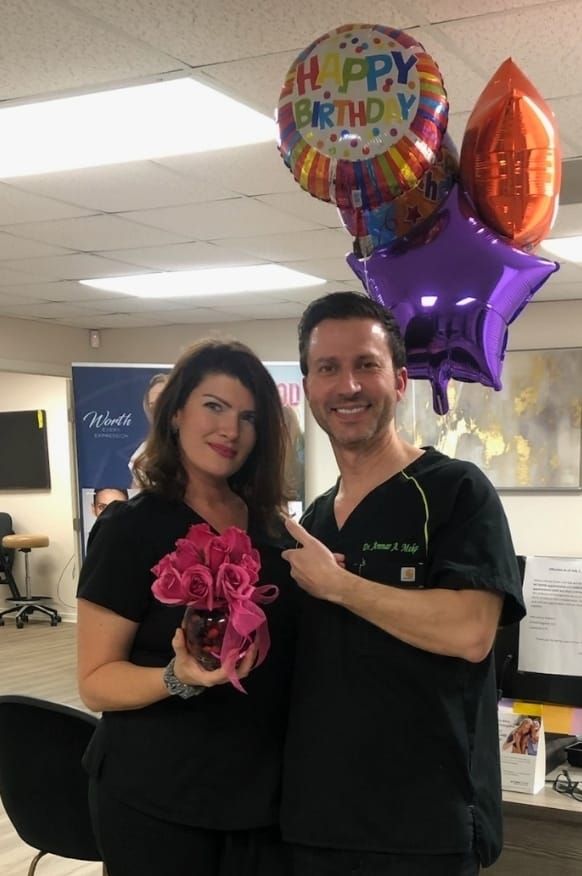 Woman holding pink roses, man pointing, both with Happy Birthday balloons.
