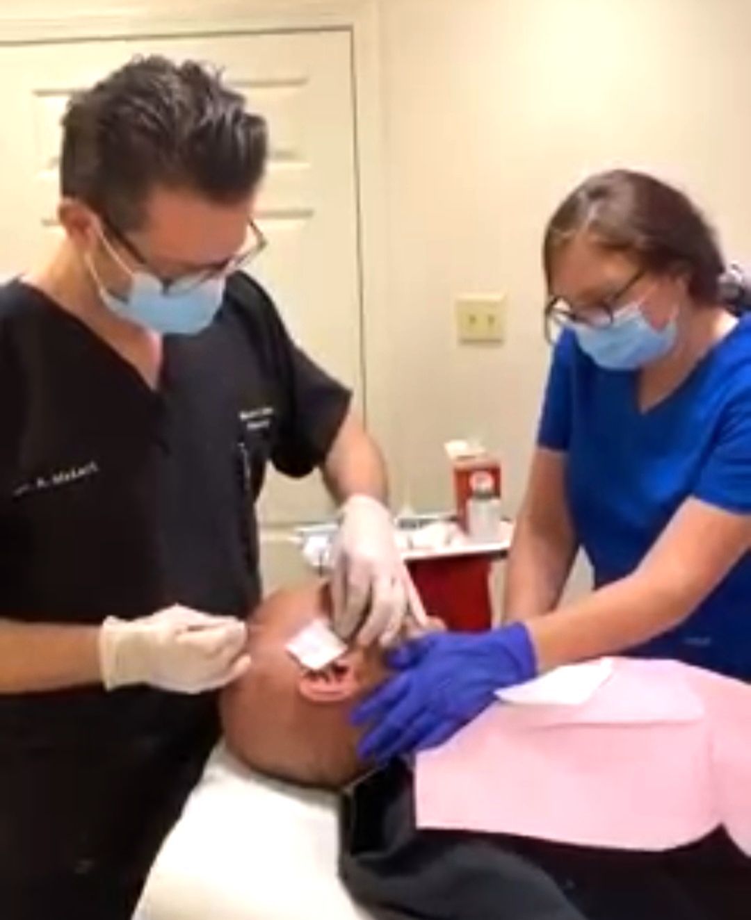 Two healthcare workers perform a procedure on a patient in a medical setting.