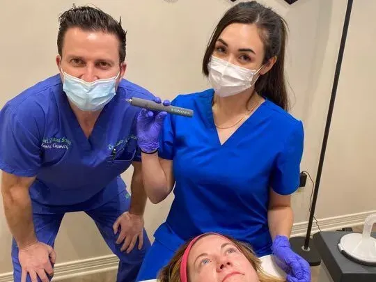 Two medical professionals in blue scrubs hold a skin care device over a patient.