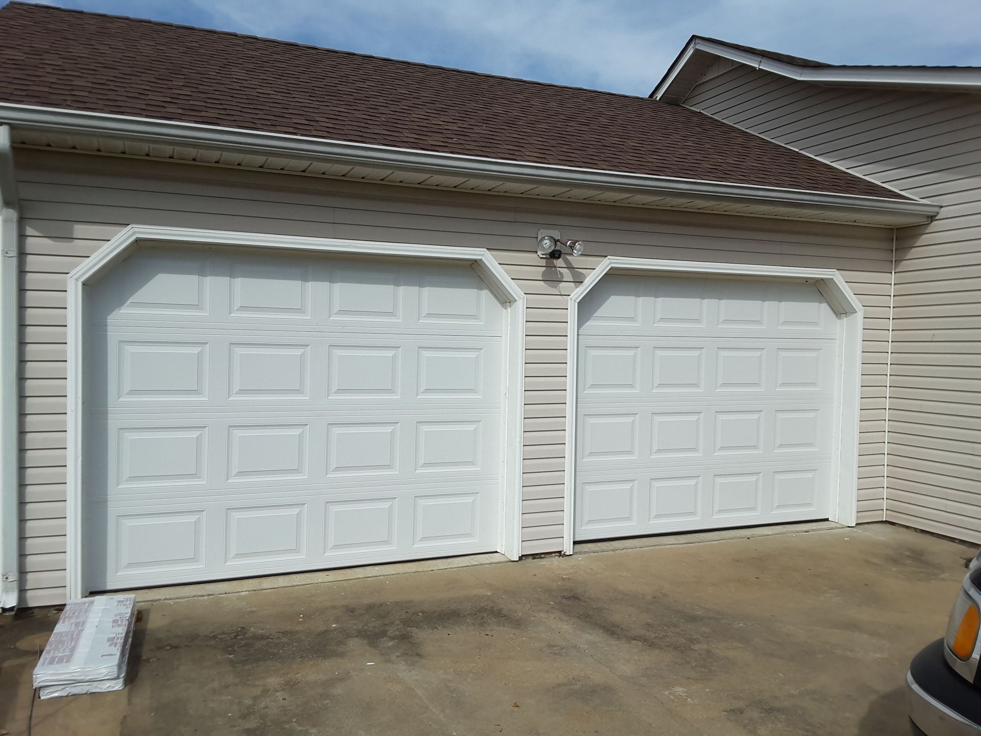 Two white garage doors on a beige house with a concrete driveway and brown shingled roof