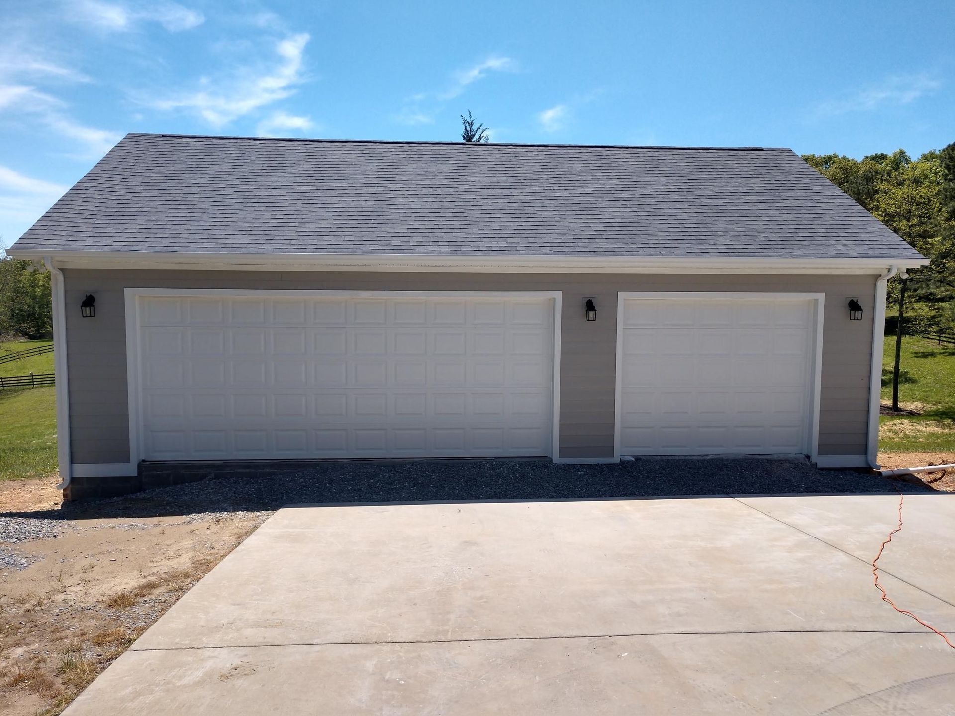 Two white garage doors on a gray detached garage with a concrete driveway under a blue sky
