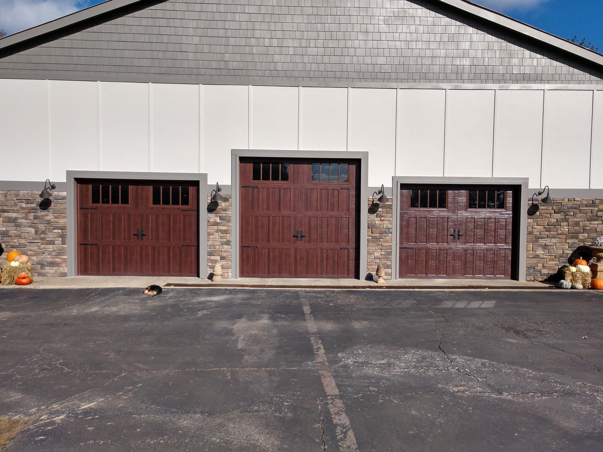 Three garage doors on a building with stone sides and a dark asphalt driveway in front.
