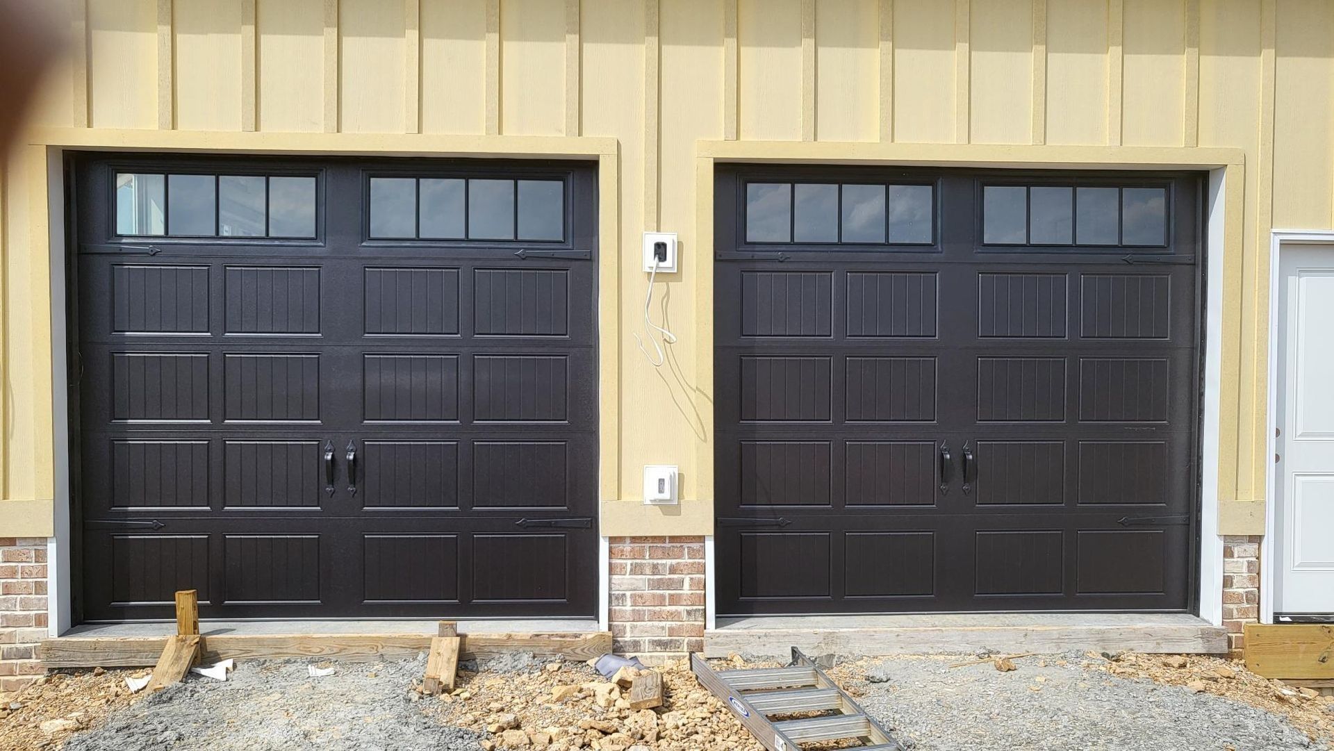 Two dark brown garage doors on a beige building exterior with gravel and a small walkway.