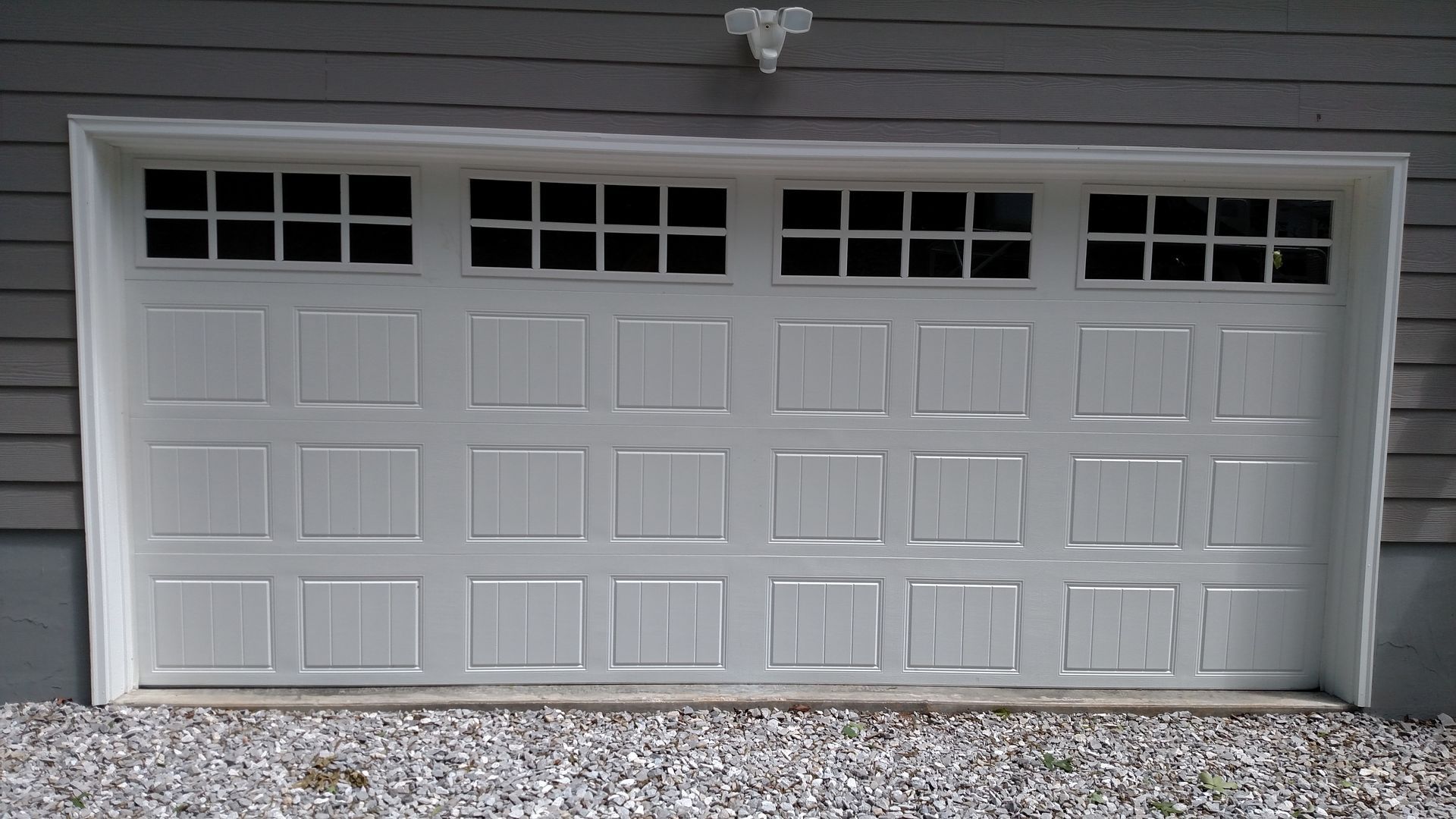White double garage door with small windows under a house exterior, above a gravel driveway.