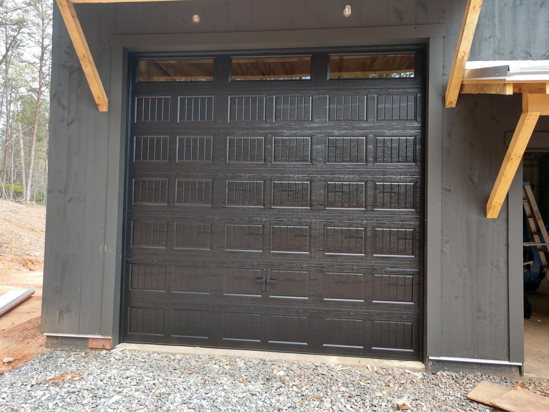 Black garage door on a dark gray building with wooden beams, viewed from outside.