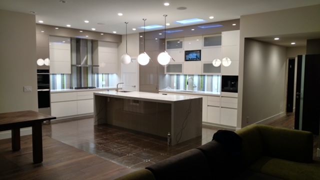 Modern kitchen with white cabinets, island, globe pendant lights, and brown flooring.