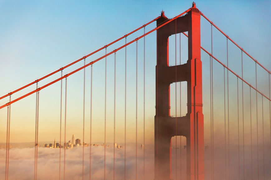 Golden Gate Bridge, San Francisco, with red tower, cables, and city skyline in the distance, partially obscured by fog.