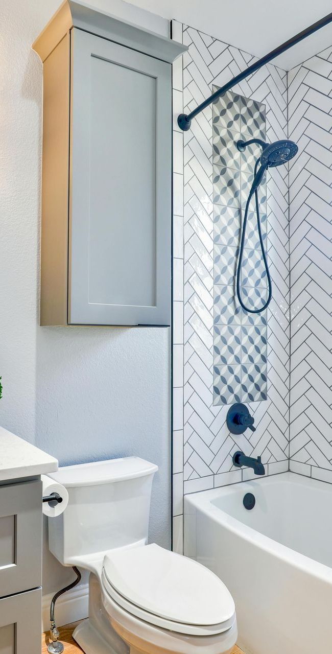 Bathroom with toilet, tub, and shower with gray and white tile. Tall cabinet above toilet.