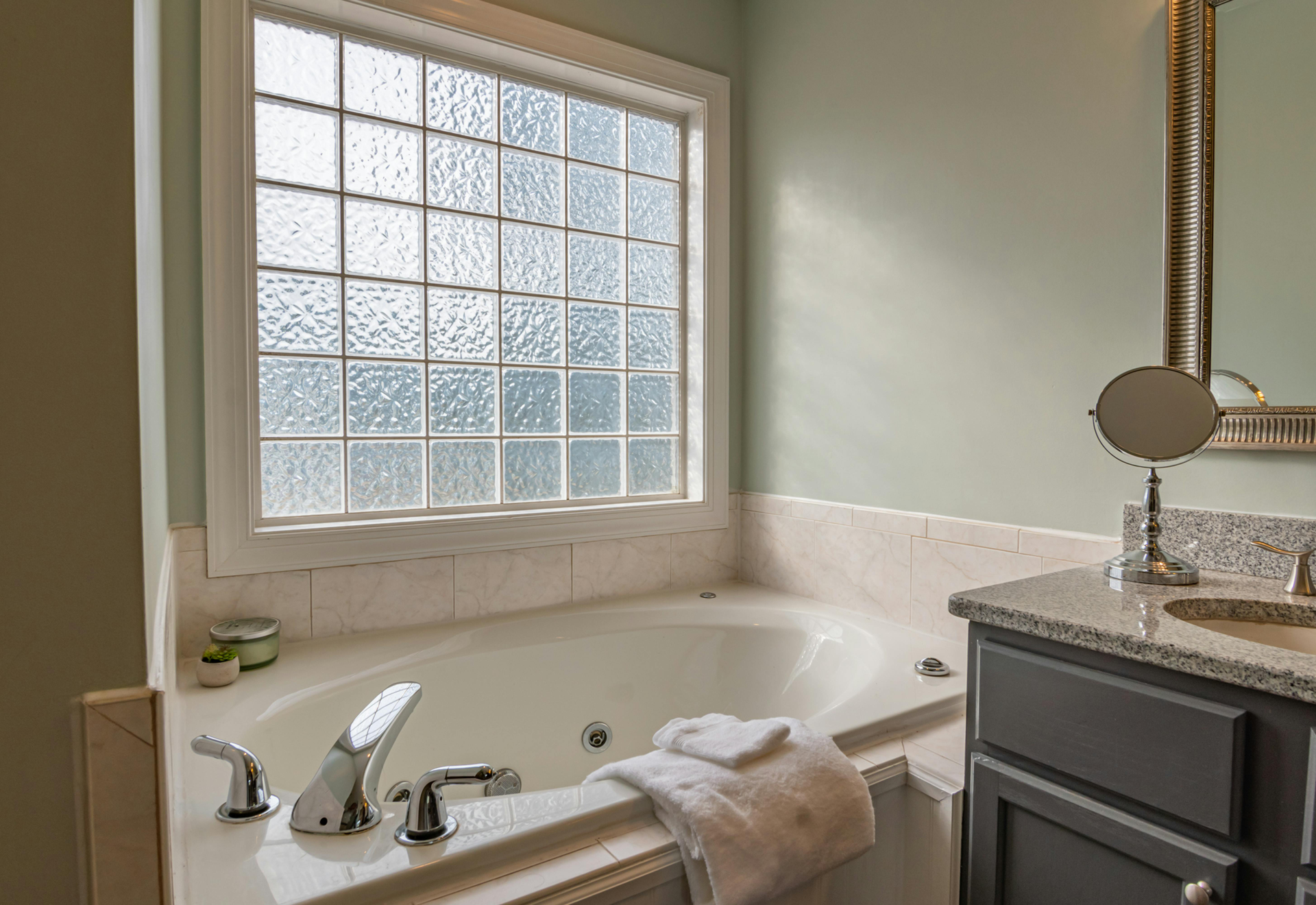 Bathroom with a white bathtub, frosted window, and a gray vanity with a mirror.
