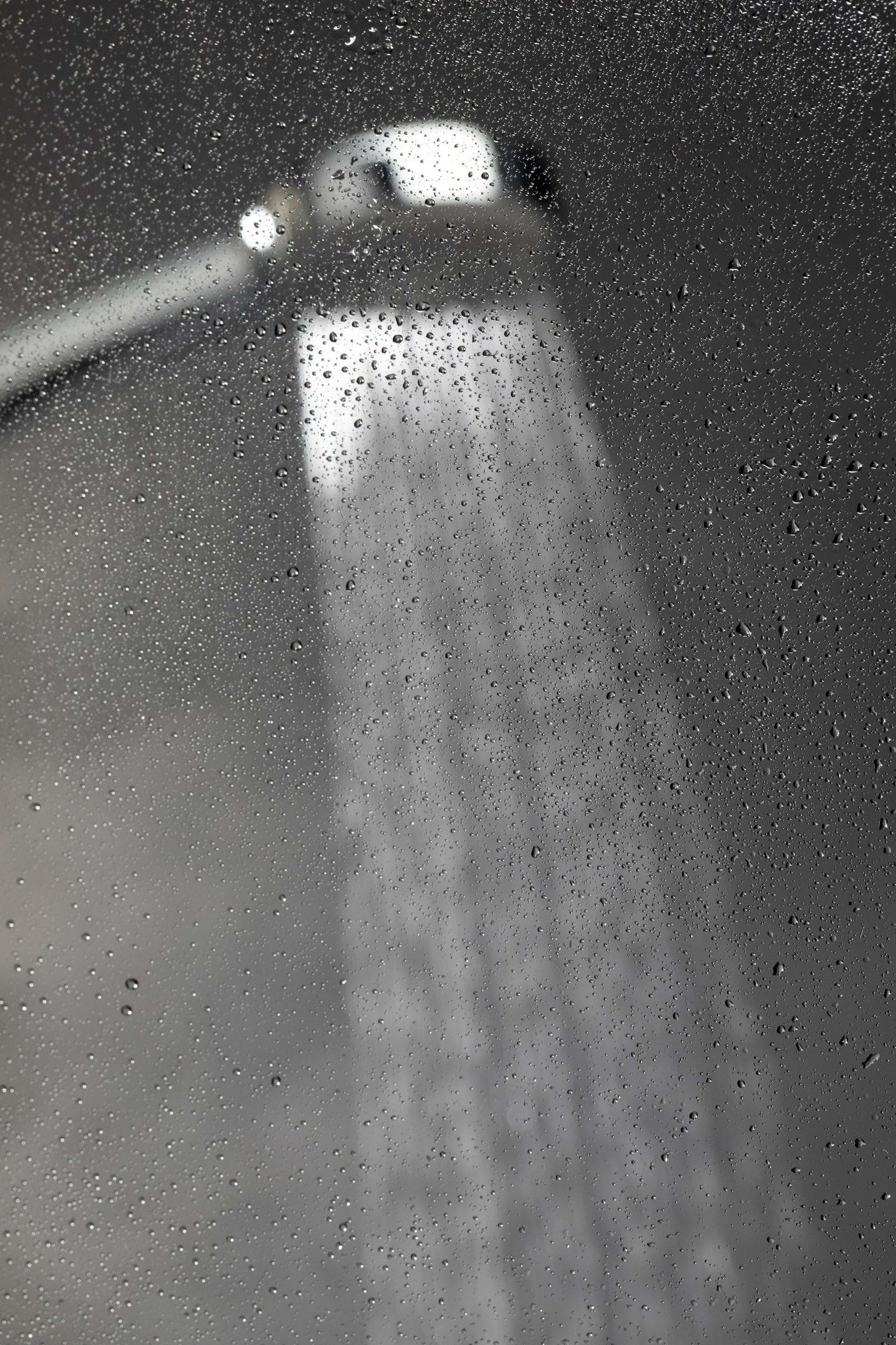 Showerhead spraying water with visible droplets on glass.