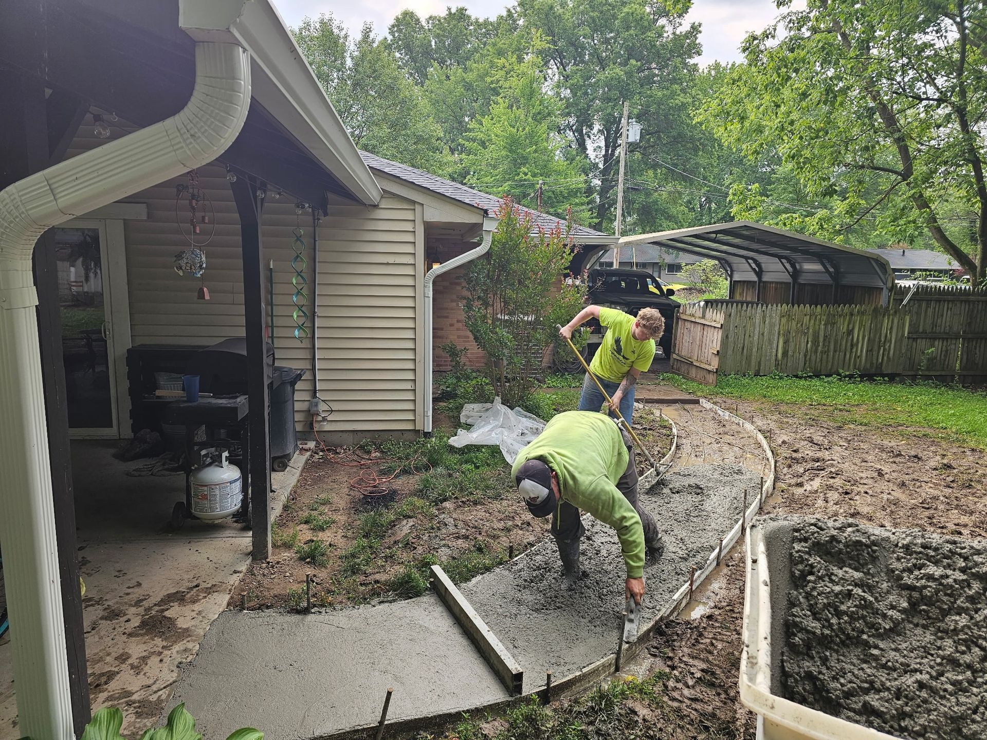 Two men are working on a concrete walkway in front of a house.