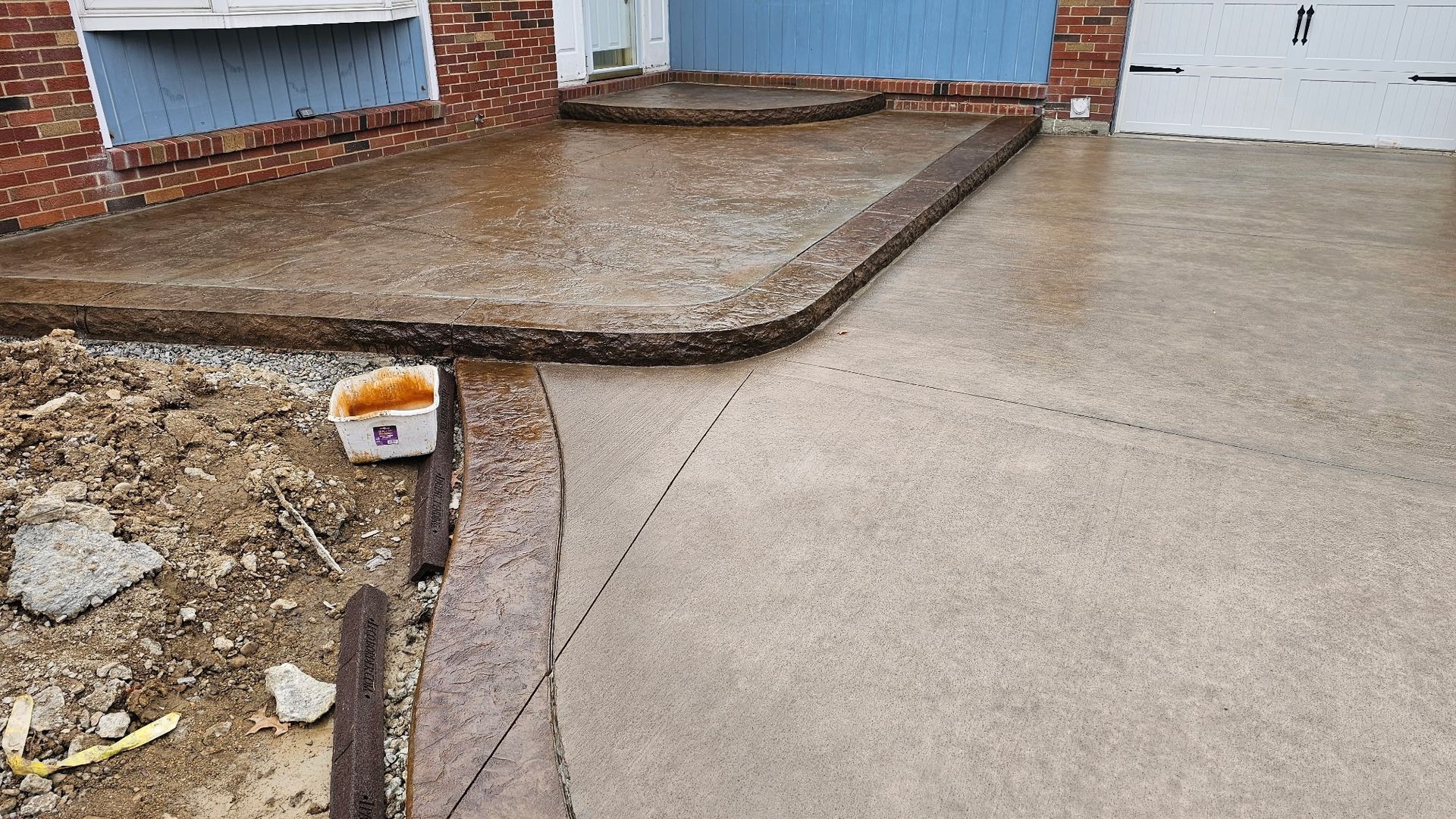 A decorative concrete driveway is being built in front of a brick house.