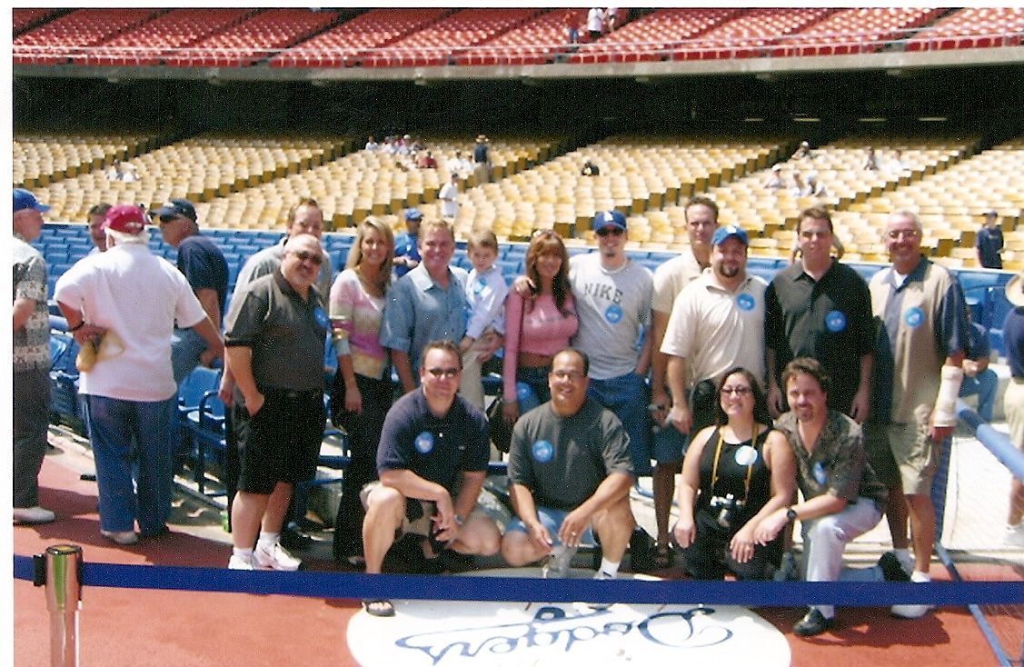 Group of people posing on a stadium field behind a blue rope, with red seats in the background.