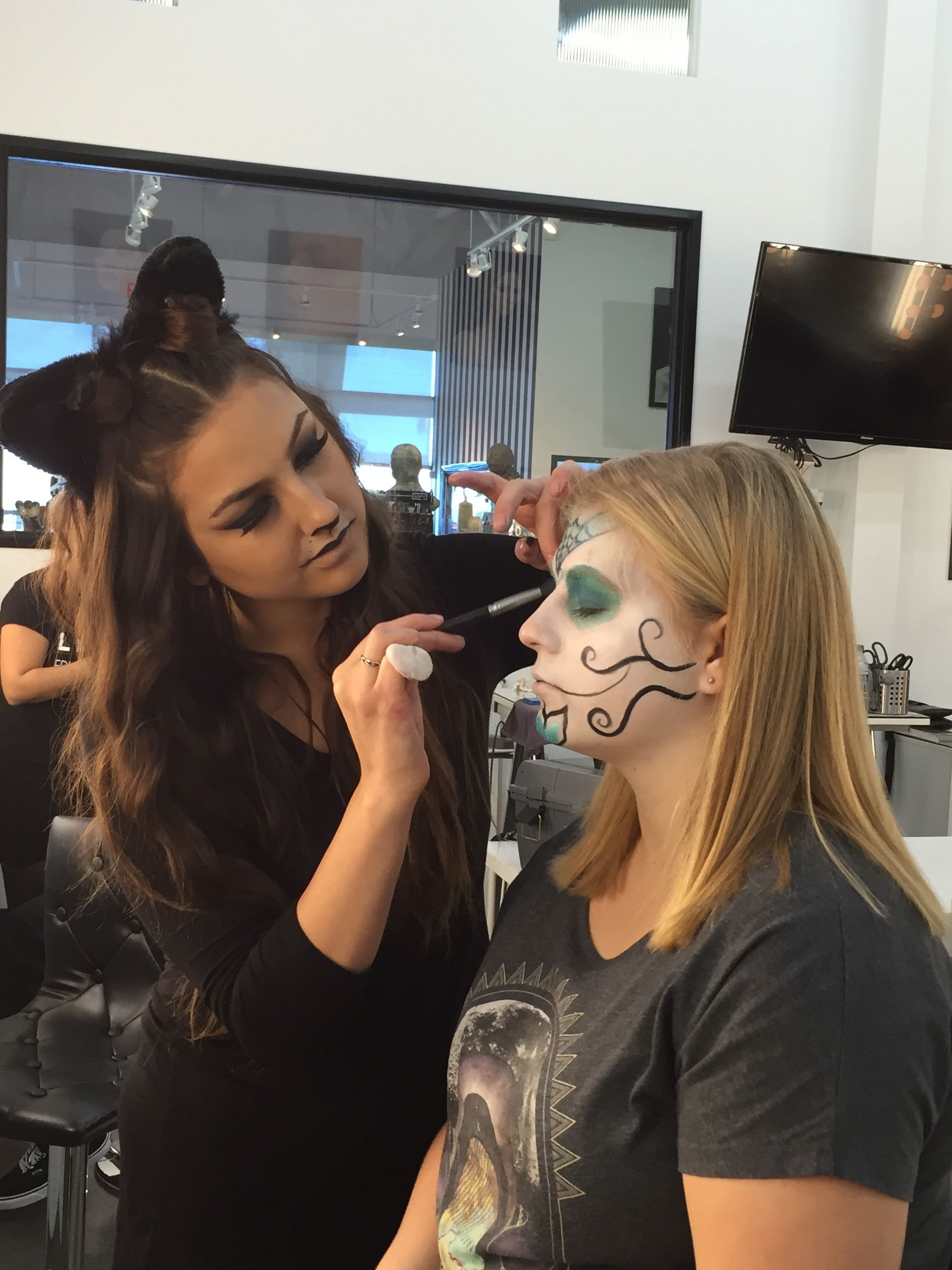 Makeup artist applying face paint to a seated person in a salon mirror area