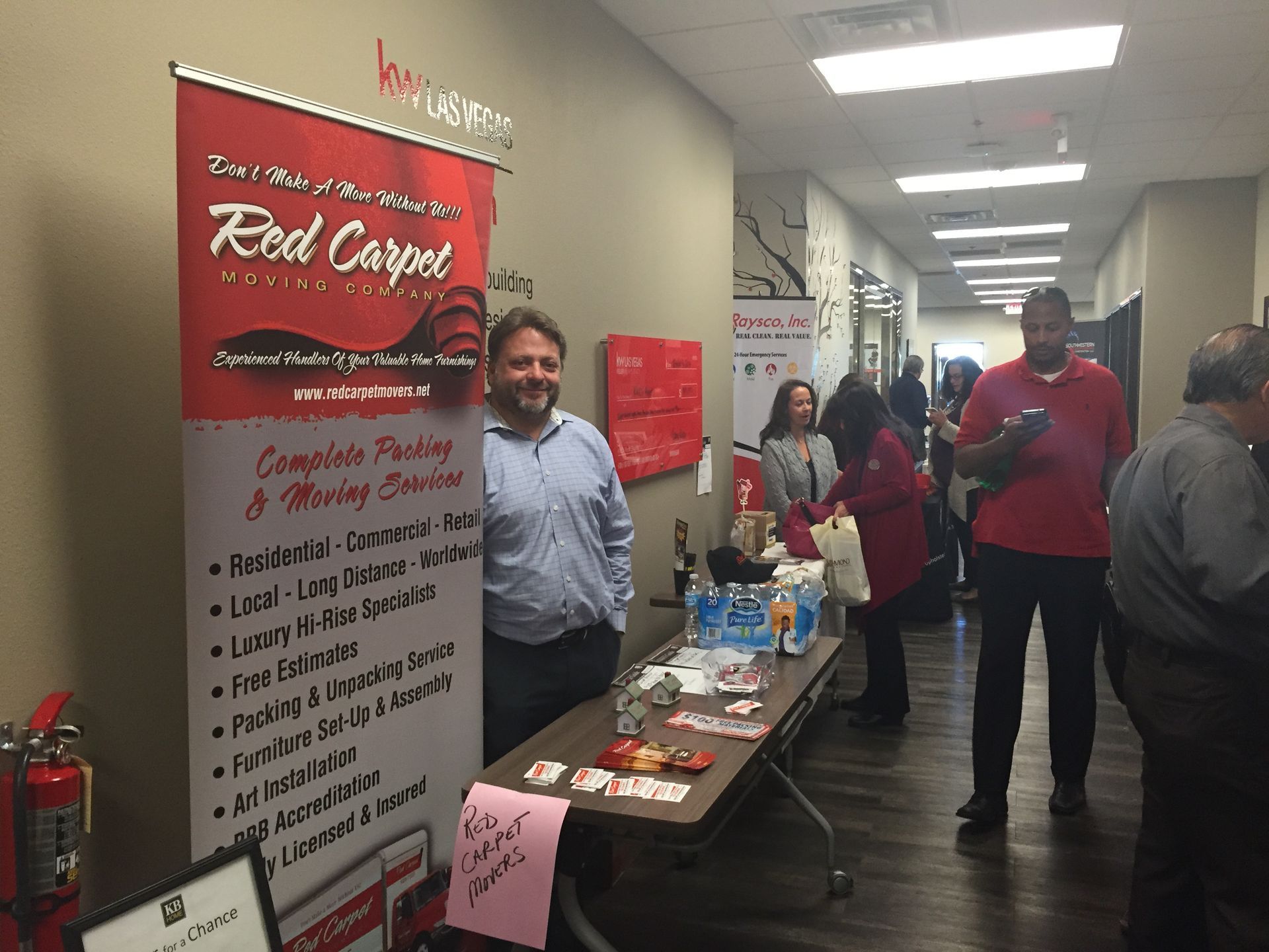 Indoor hallway booth with a red banner, brochures, and people talking at a community event
