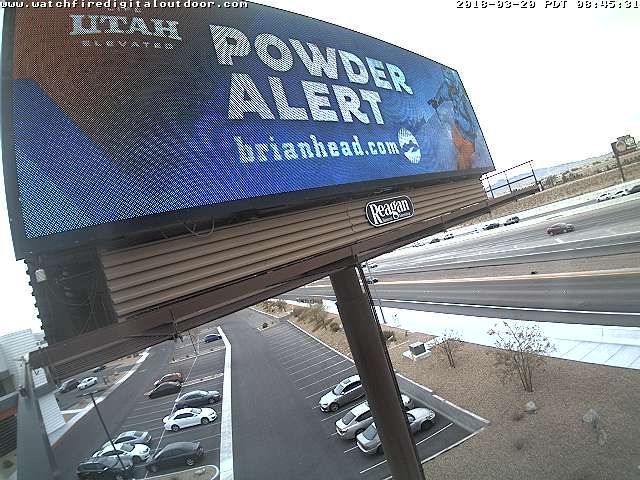 Billboard reading “POWDER ALERT” in white text on a blue mountain-weather sign above a snowy parking lot.