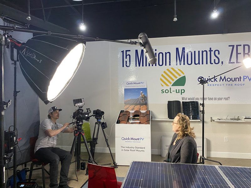 Trade show booth with camera crew filming under bright lights, featuring a “15 Main Mounts” banner.