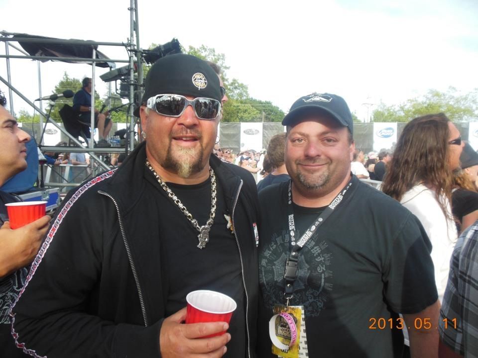 Two men in black shirts and caps smiling at an outdoor event, holding red cups.