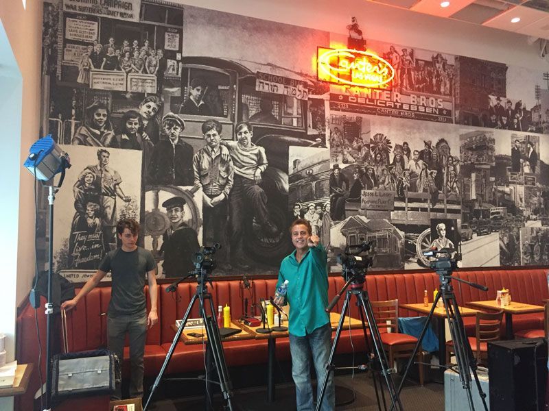 People standing with cameras in a retro diner-style room with a black-and-white mural and red neon sign.
