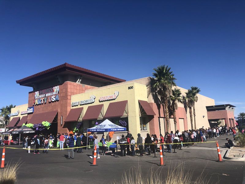 Crowd lined up outside a shopping center with a yellow facade under a clear blue sky