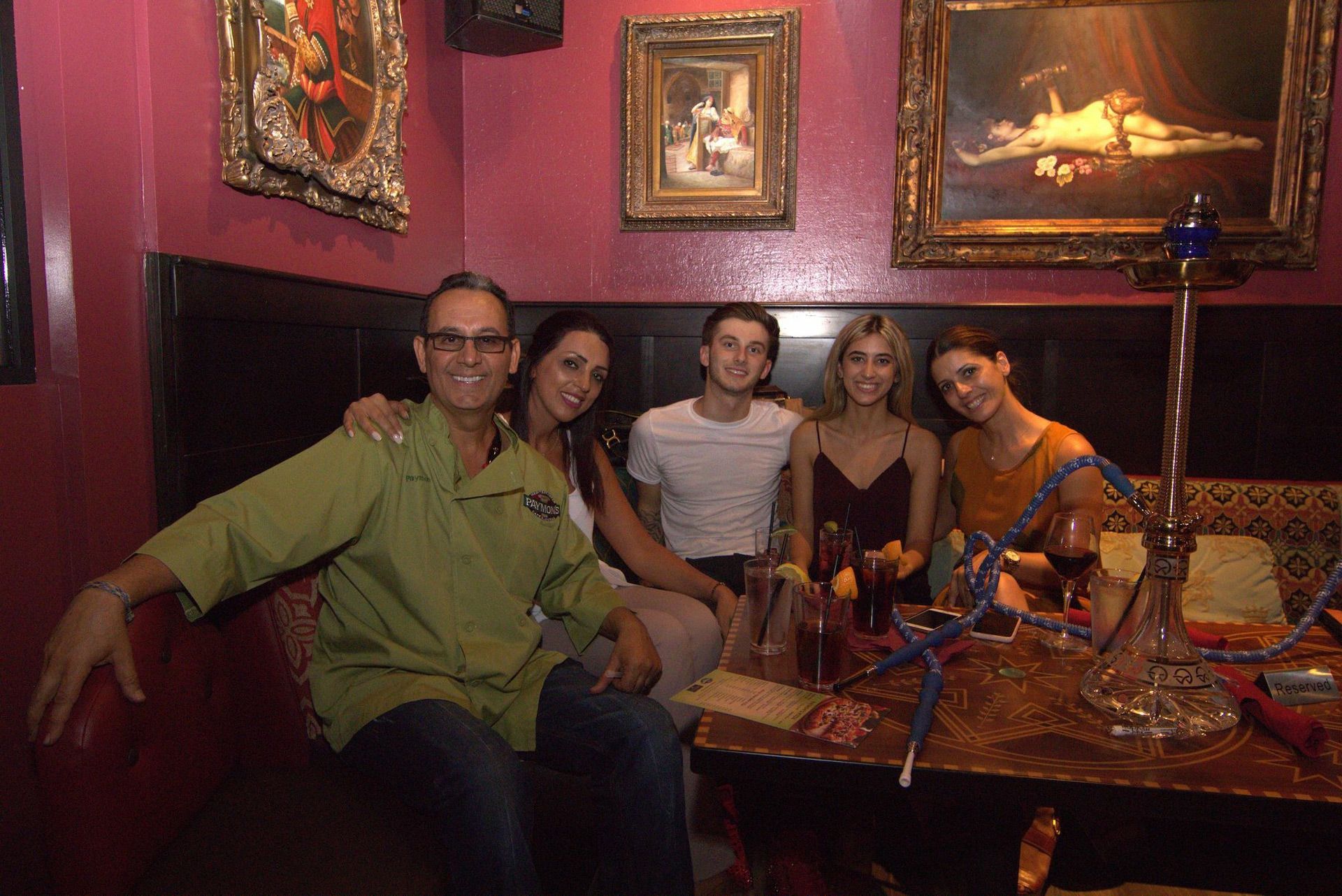 Five people sitting at a table in a dim, red-walled lounge with framed artwork and drinks