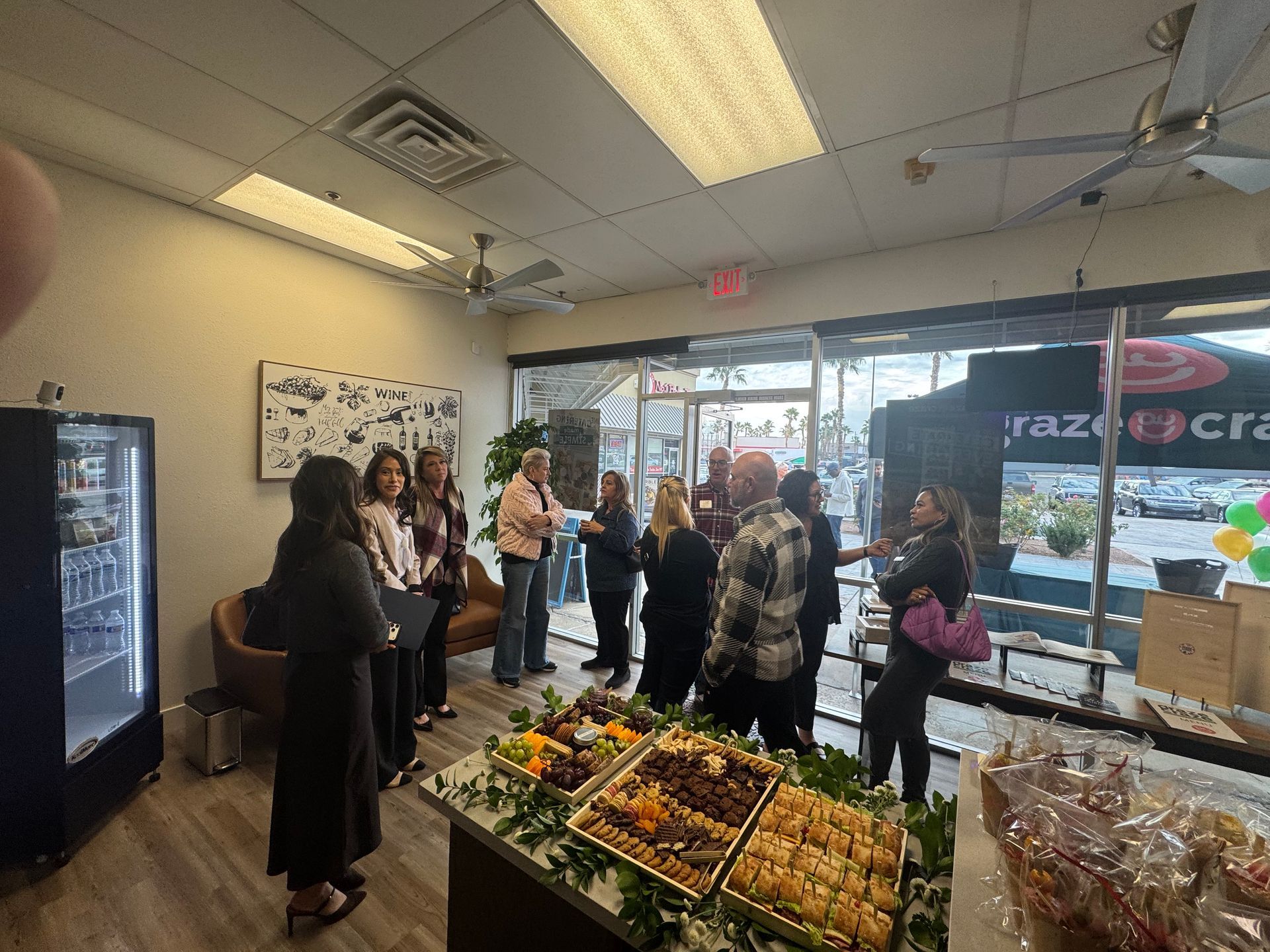 People gathered inside a produce market near a display of fruits and flowers by the window.