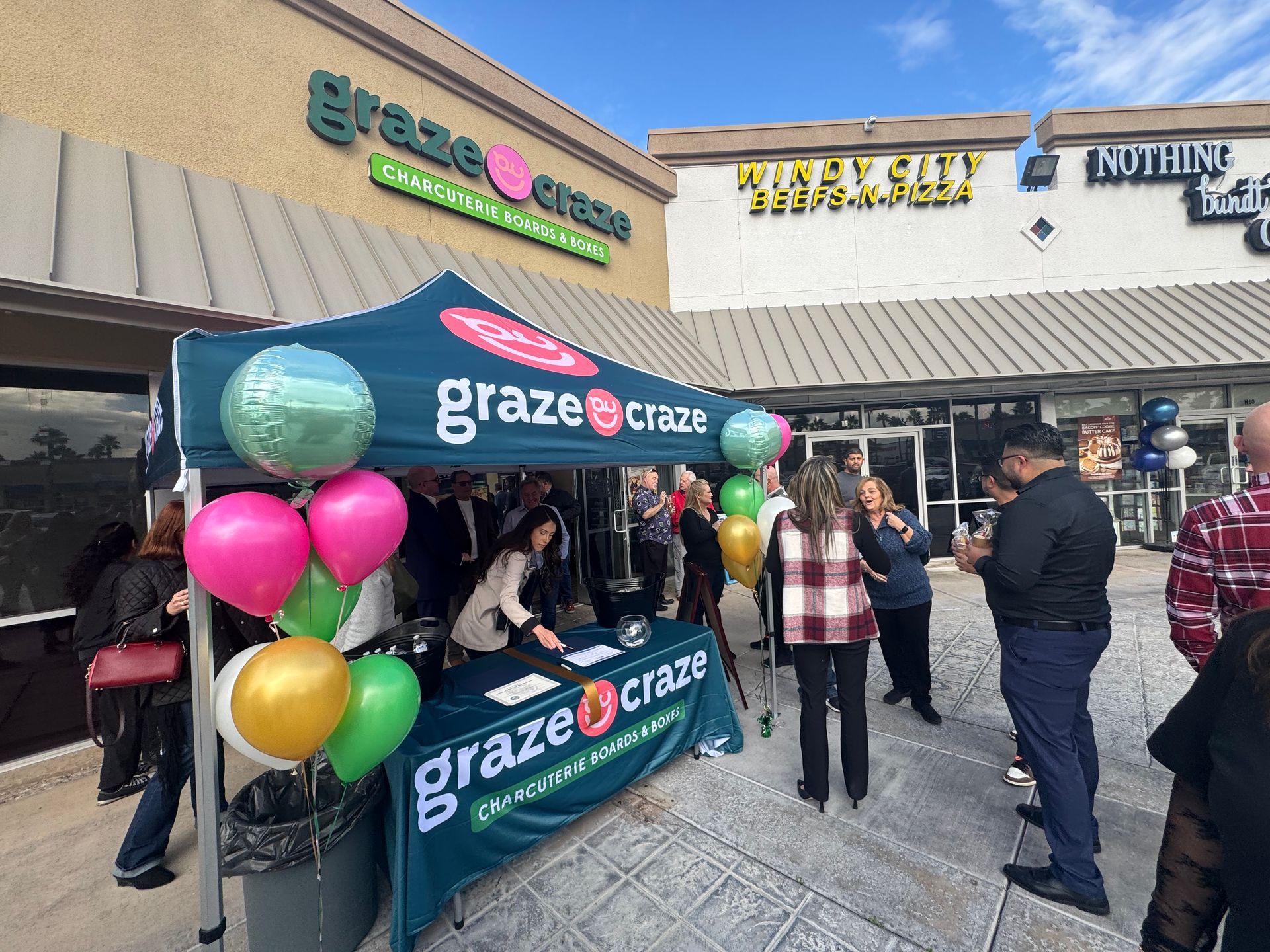Graze Craze storefront with balloons and a small crowd at an outdoor shopping center opening