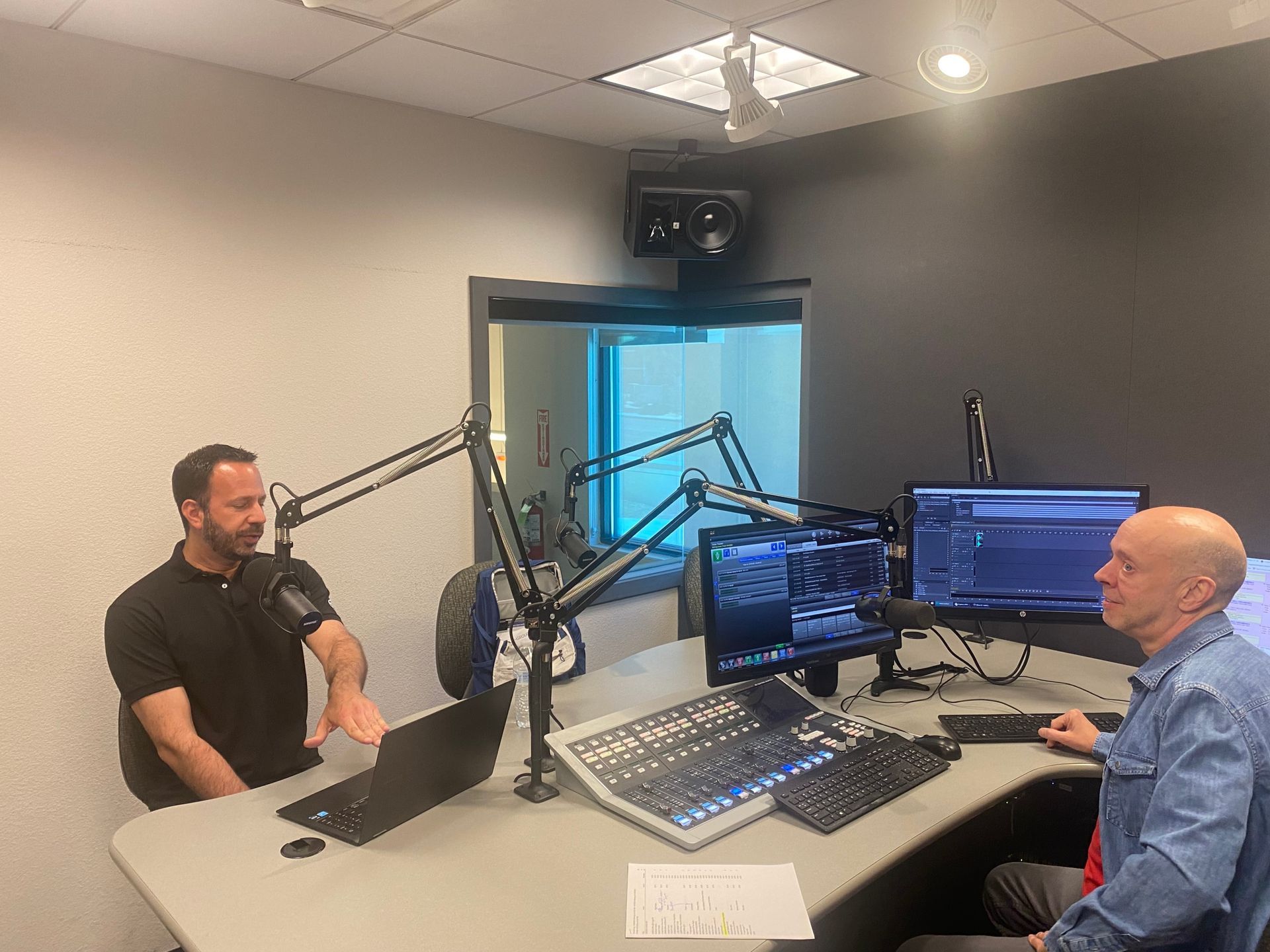 Two men in a podcast studio with microphones, headphones, and audio monitors.