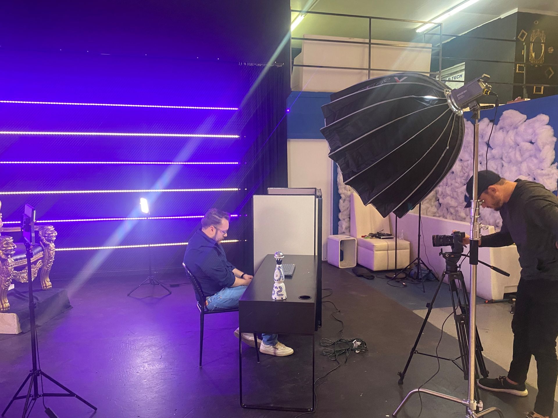 Studio photoshoot with purple lighting, softbox lights, and a person seated at a table.