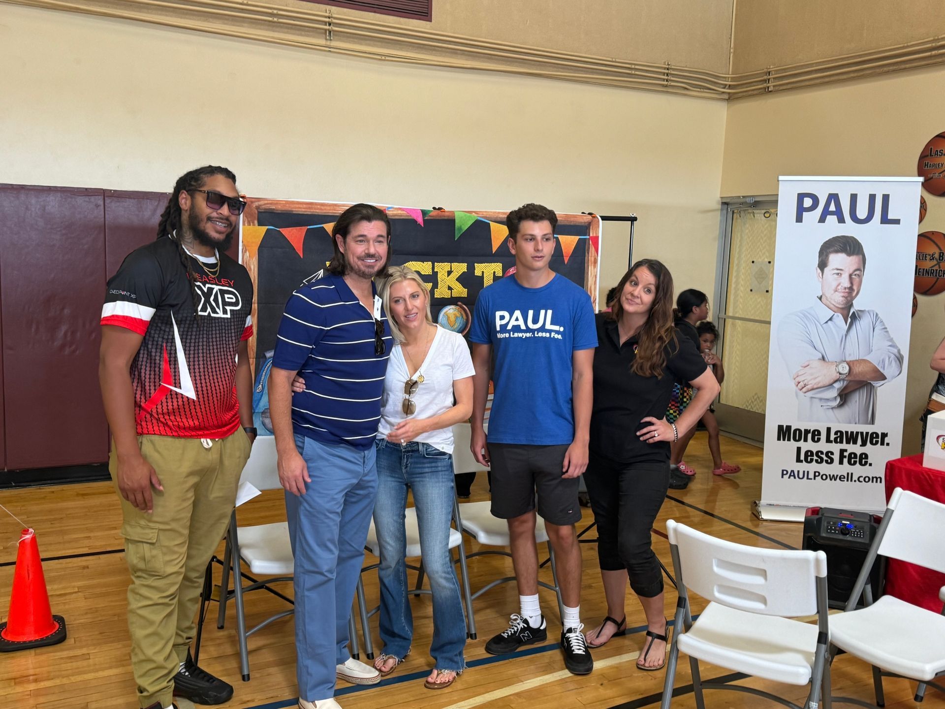 Four people posing at a booth with a PAUL campaign poster in the background.