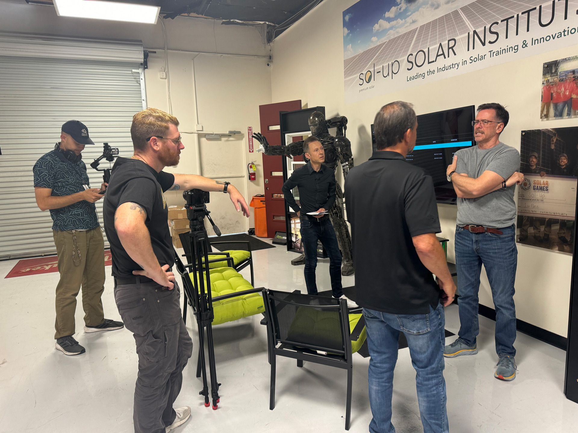 People chatting in a lab-like room with tripods, chairs, and a solar institute banner on the wall.