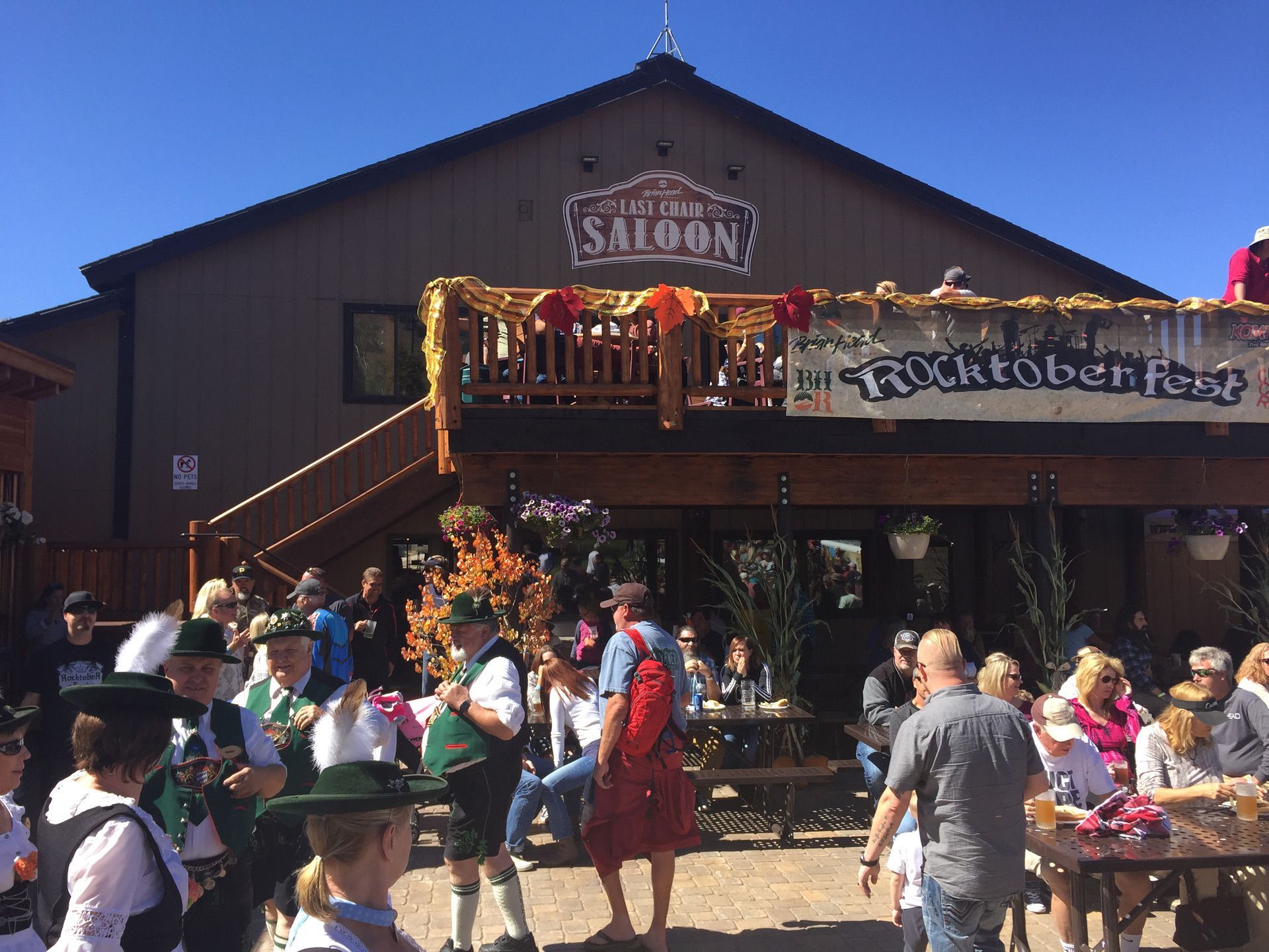 Crowded outdoor festival in front of a rustic saloon with a balcony and a “Rocktoberfest” banner.