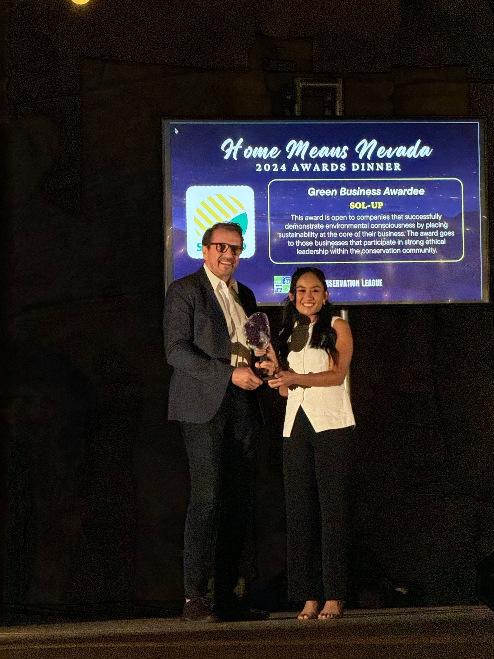 Two people onstage receiving an award in front of a large event screen