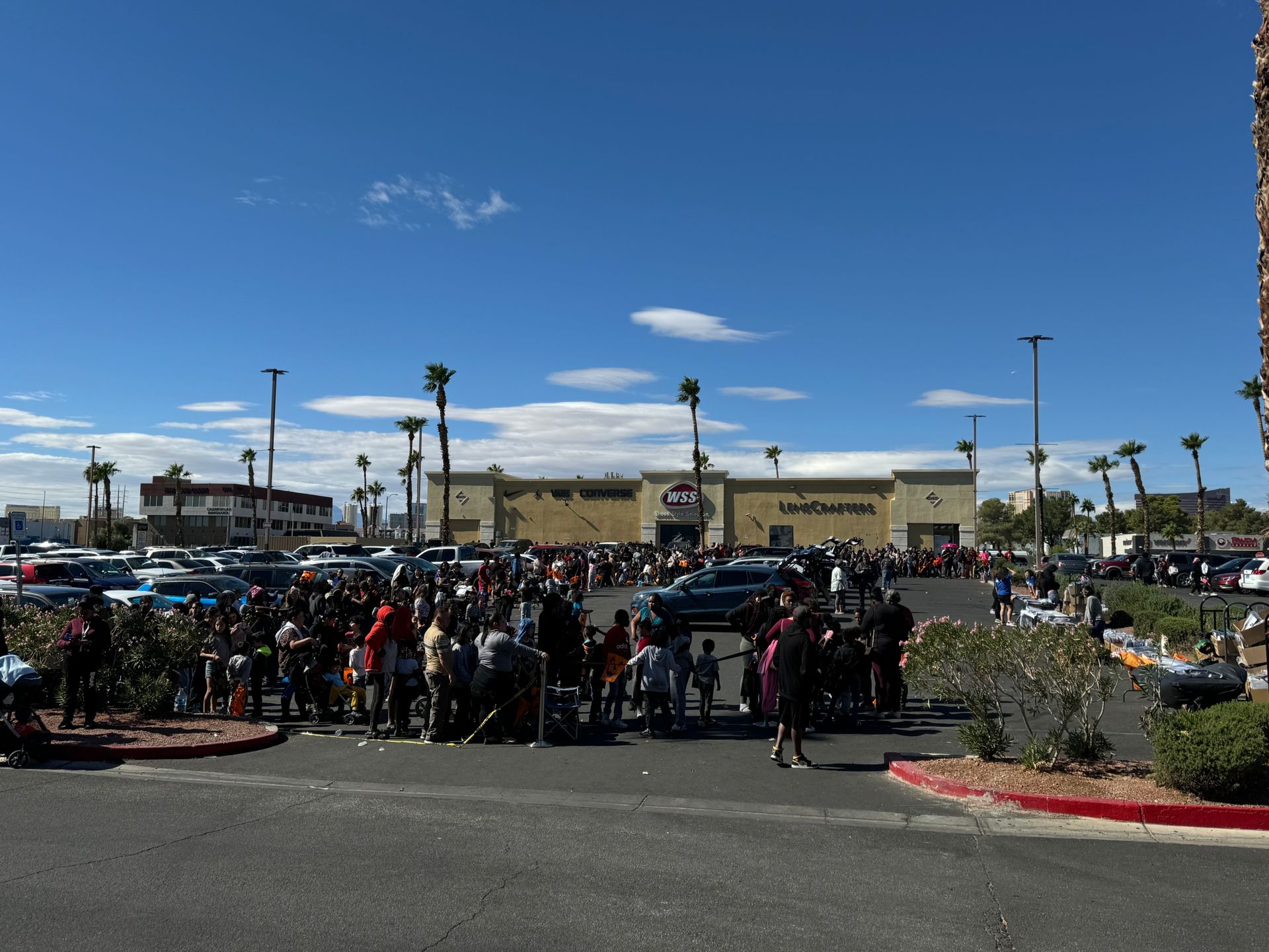 Crowd gathered in a parking lot outside a shopping center under a clear blue sky
