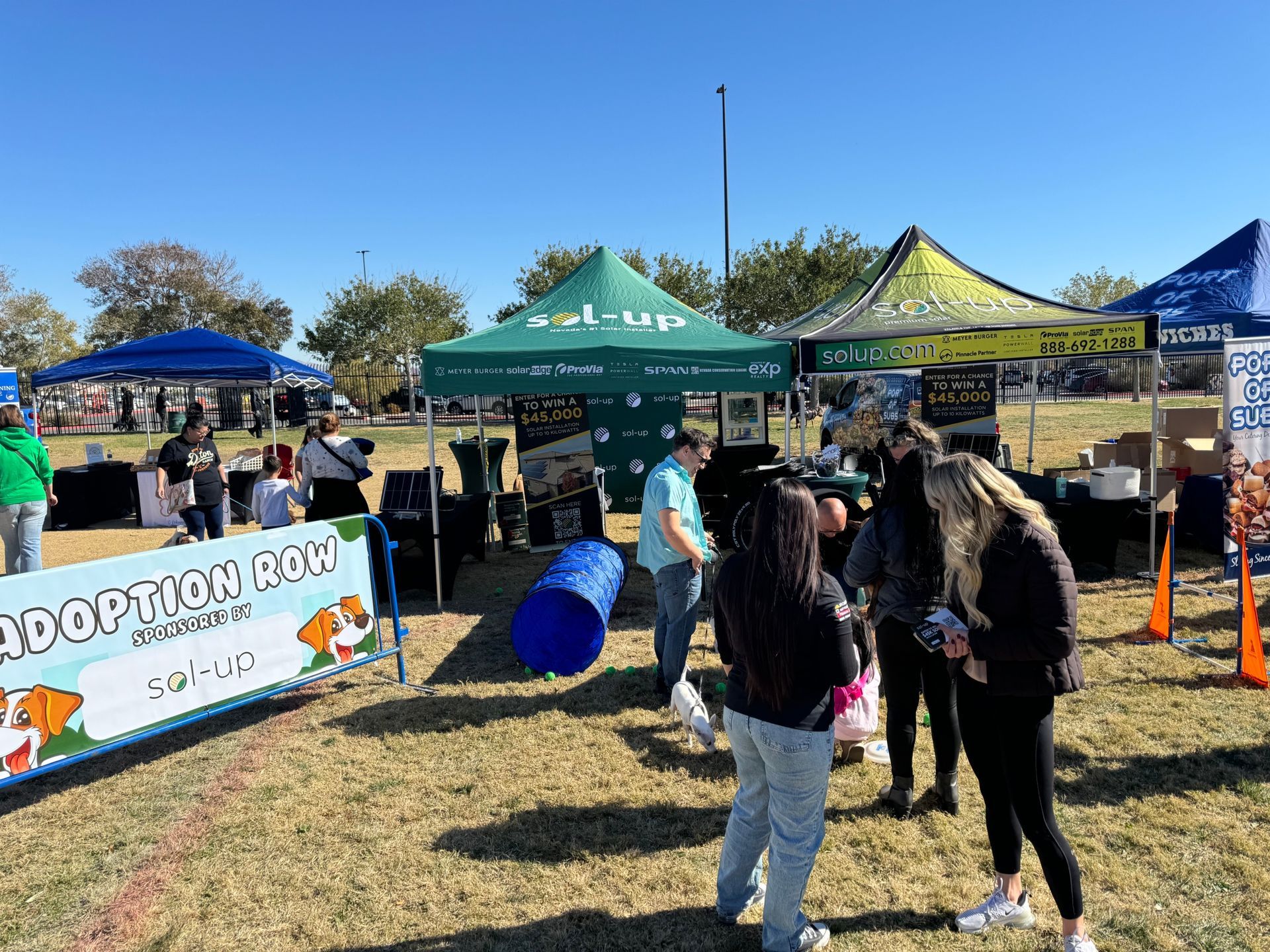 Outdoor food and vendor tents at a community event, with people browsing under colorful canopies.