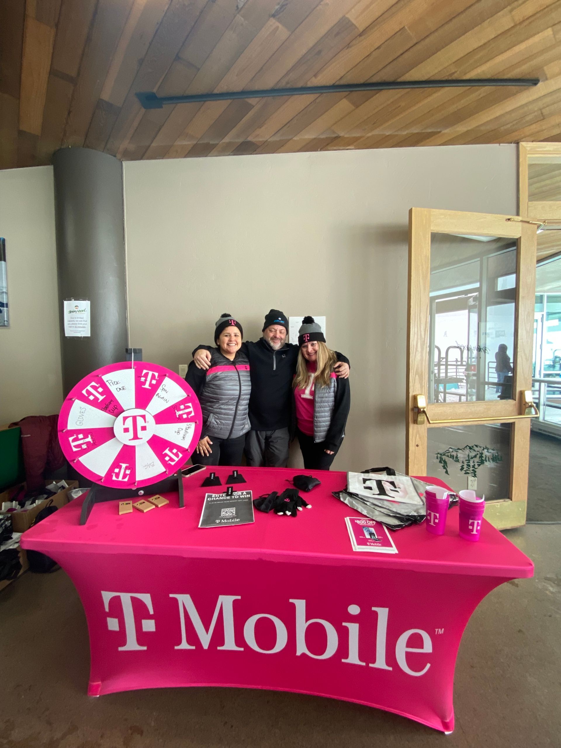 T-Mobile booth with pink tablecloth, prize wheel, and two people standing behind the table indoors