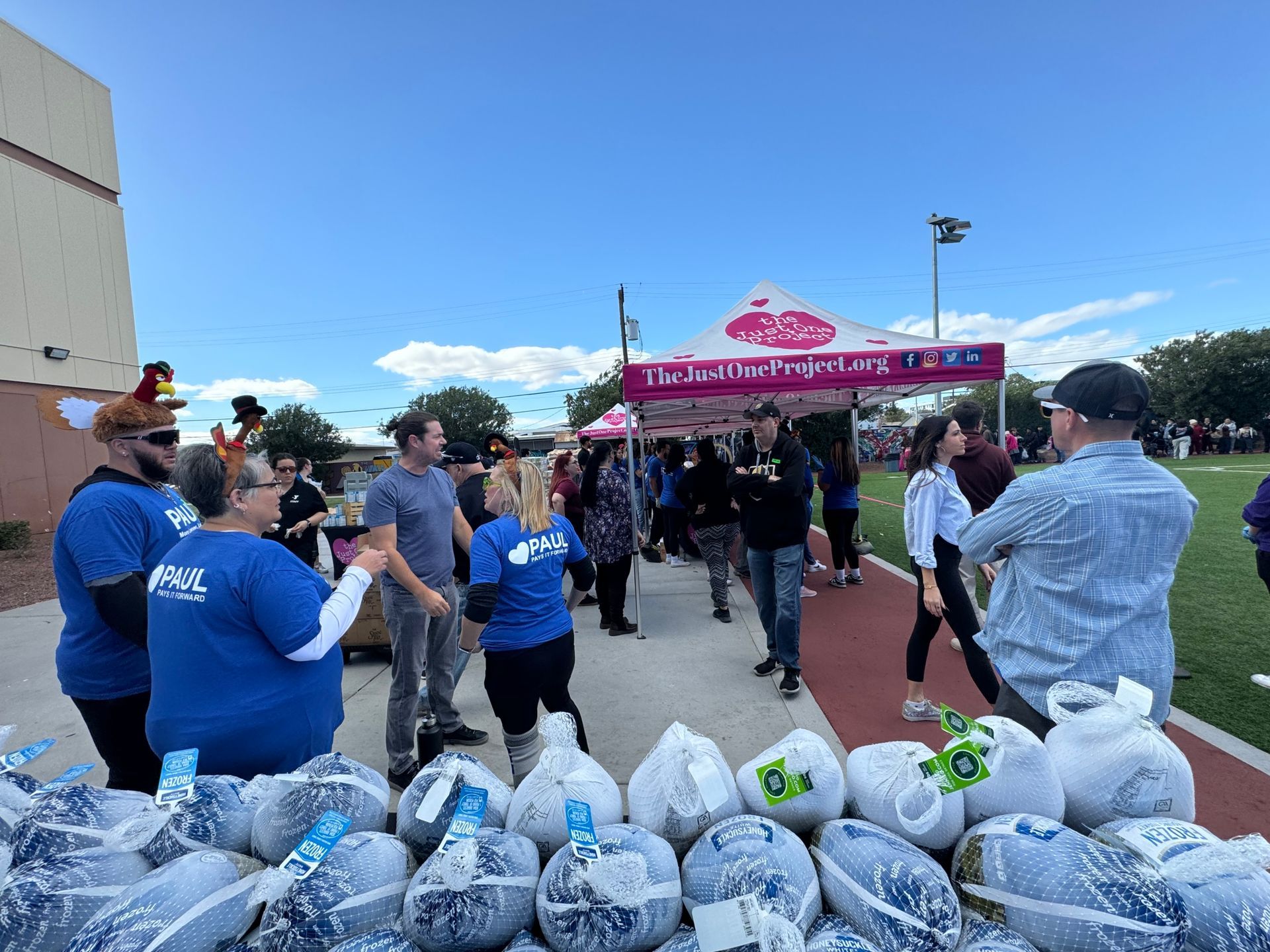 Volunteers at a pink canopy tent distribute blue bags outdoors on a sunny day