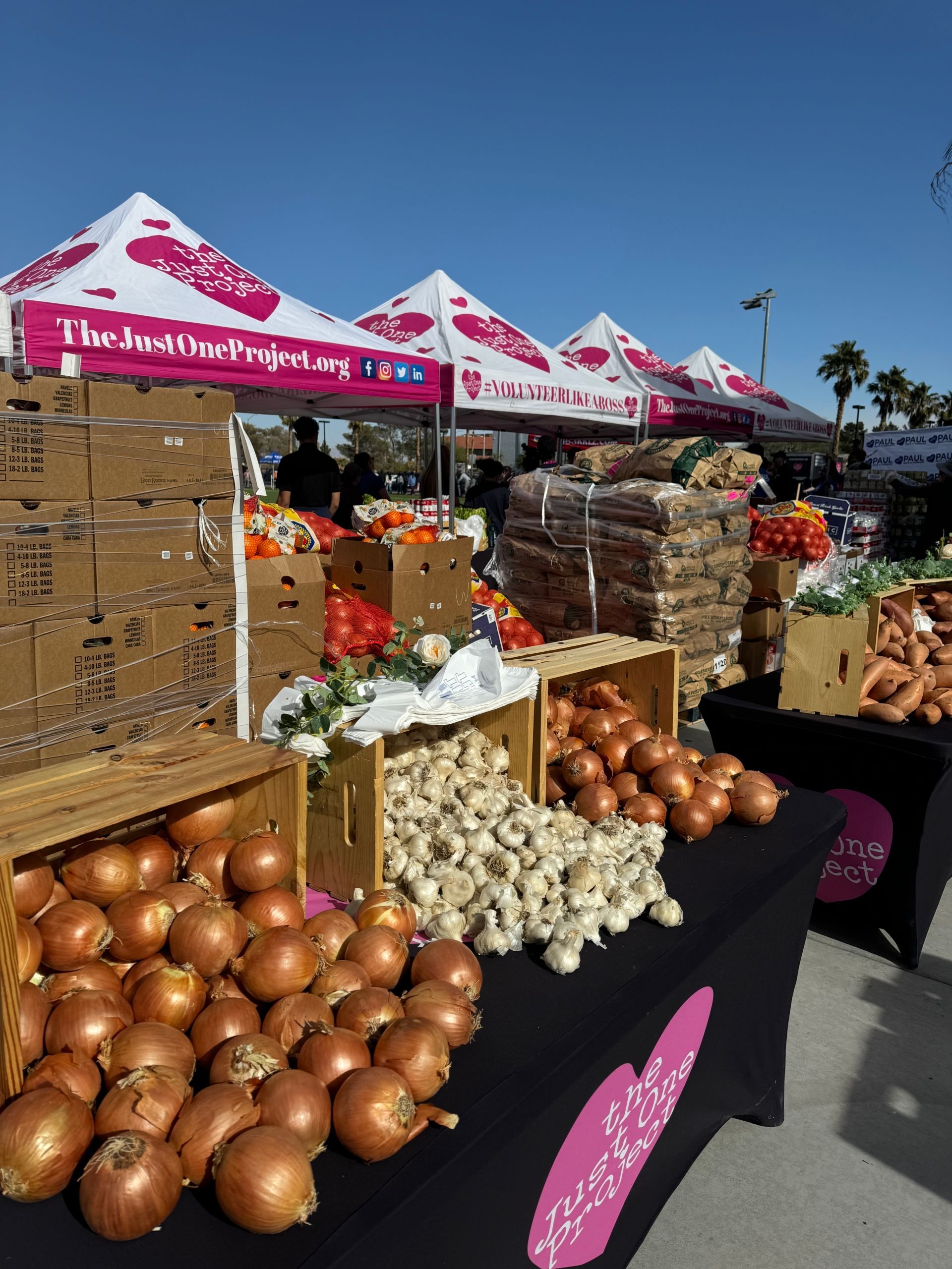 Outdoor produce stand with onions, garlic, and bread under pink-and-white tents at a market