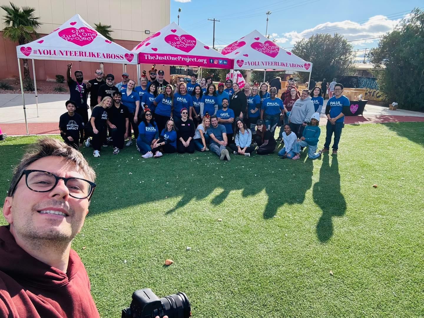 Group selfie of people posing on a grassy lawn under pink branded tents outdoors