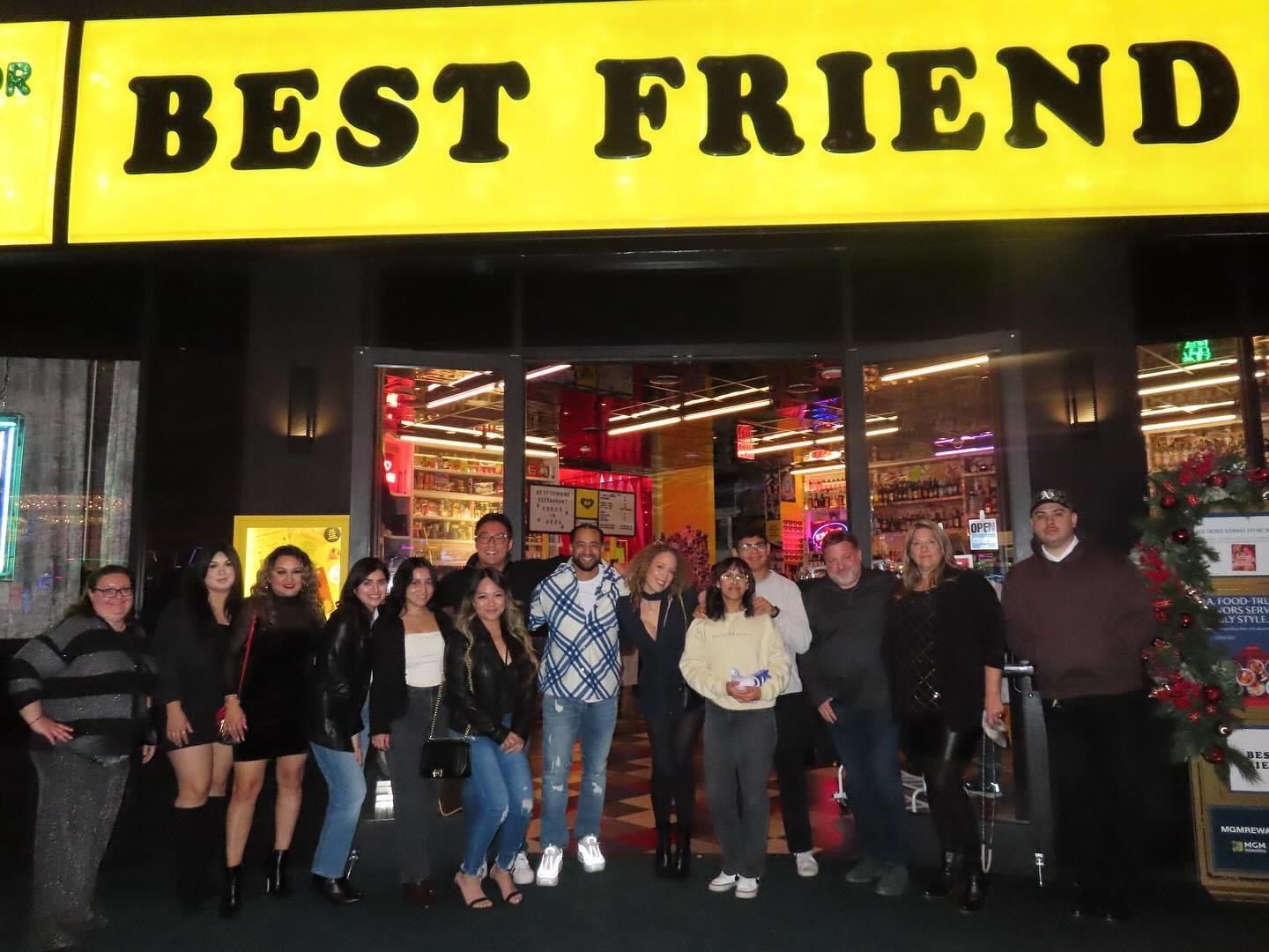 Group posing outside Best Friend restaurant at night under a bright yellow sign
