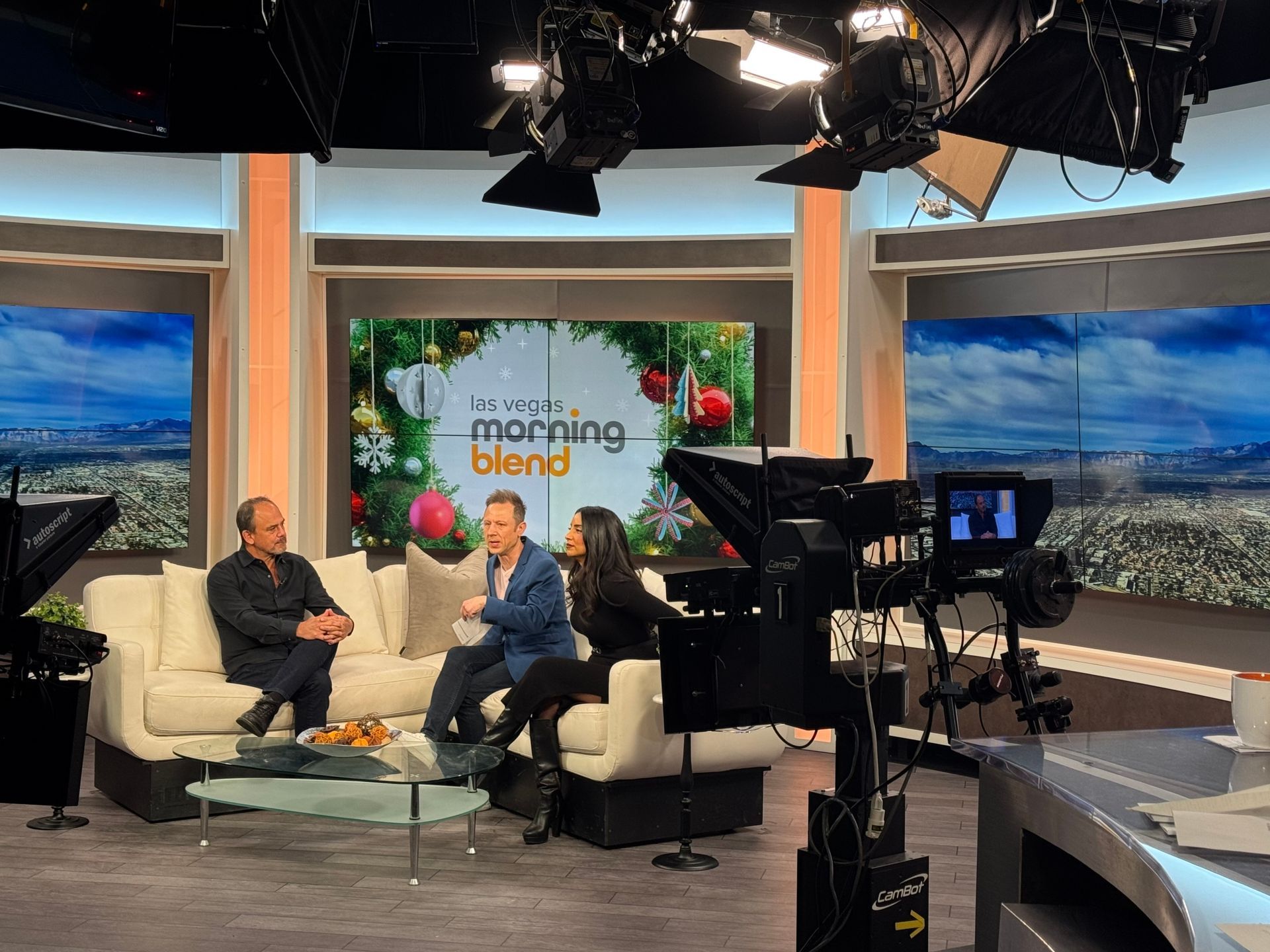 Two people chatting on a white sofa in a TV studio set with cameras, lights, and “Morning Blend” backdrop.