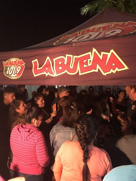 Crowd gathered under a red LA BUENA radio tent at a nighttime outdoor event